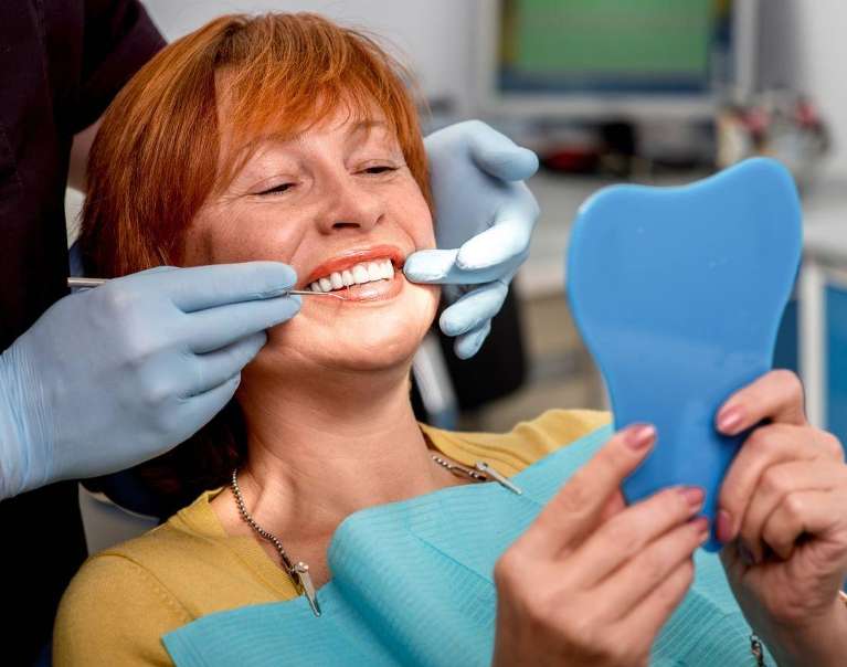 woman sitting in a dental chair while holding a mirror