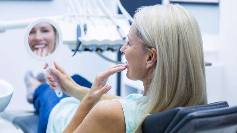 woman smiling into dental mirror in evansville